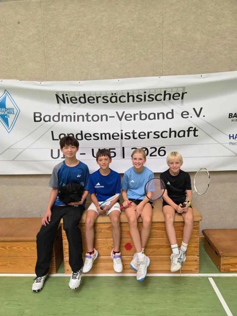 Vier Kinder des BC 82 sitzen mit ihren Badmintonschlägern vor dem Banner der Landesmeisterschaft U11 bis U15 2026.
